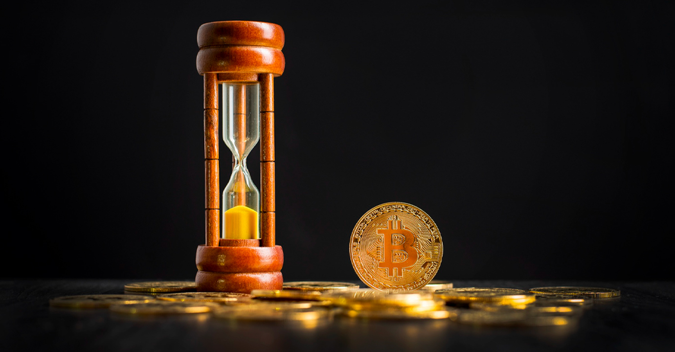 Clessidra e moneta con logo di bitcoin sopra tante monete